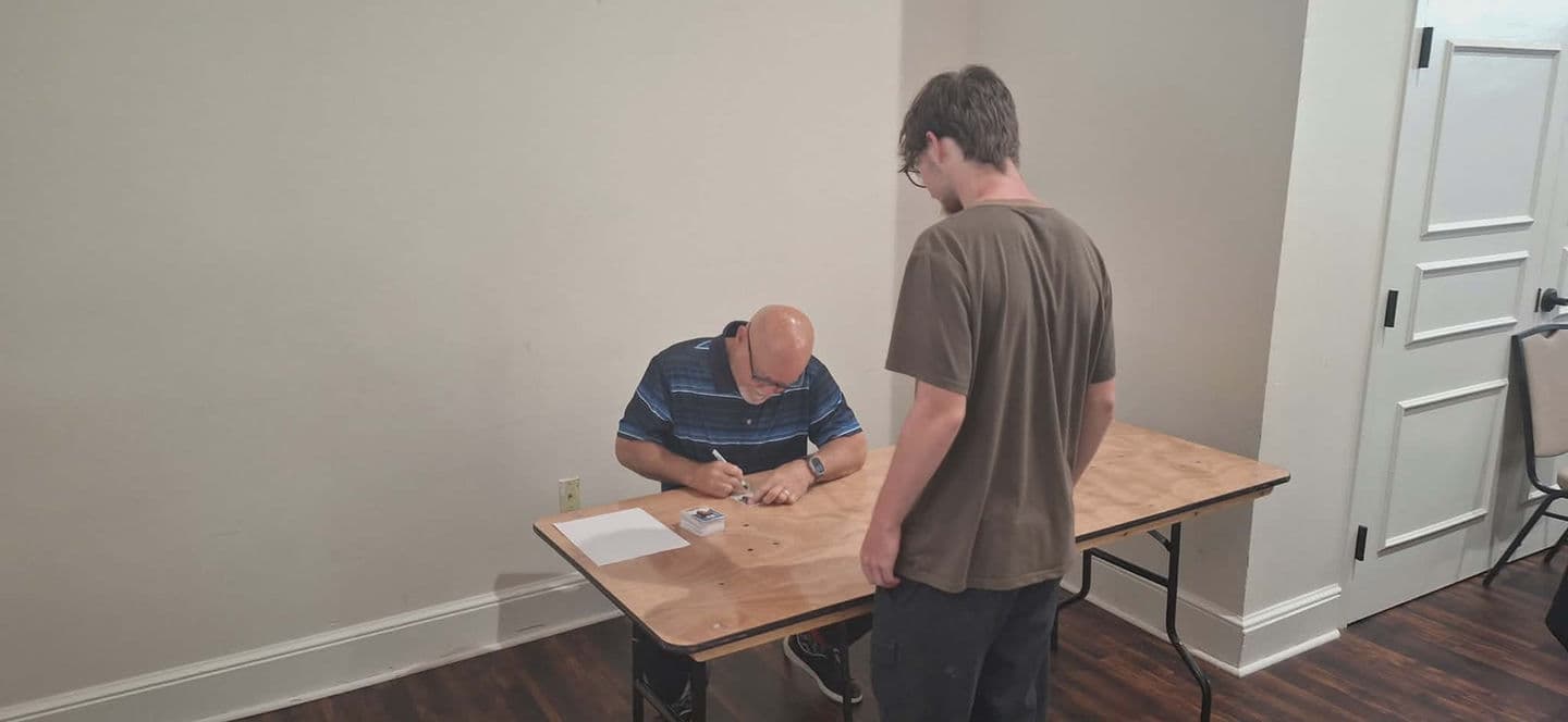 A dealer checking in a collector's cards across a setup table